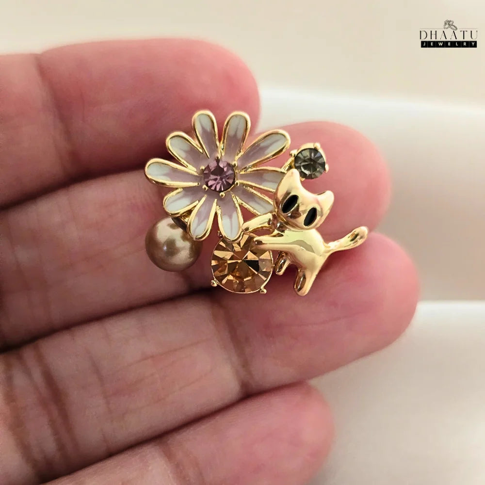 A close-up shot of the DHAATU JEWELRY gold-toned playful cat and floral adjustable ring, highlighting the detailed enamel flower, champagne rhinestone, and pearl on a hand.