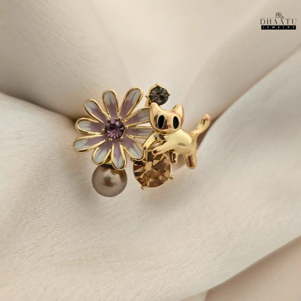 The gold-toned playful cat and flower ring shown on a light-colored fabric, allowing the intricate details and colors to stand out.