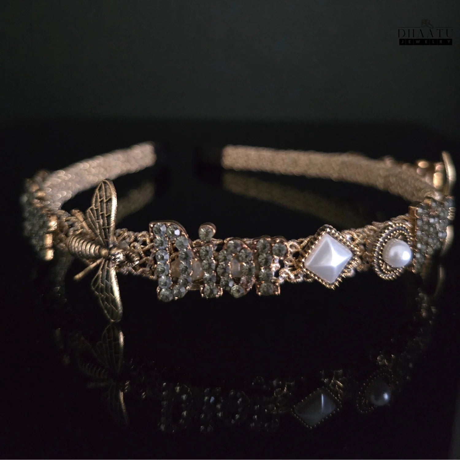 Angled view of golden hairband showing bee, "Dior" text, pearls, and square gems