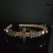 Elegant golden hairband with bee and rhinestone details against a dark reflective surface