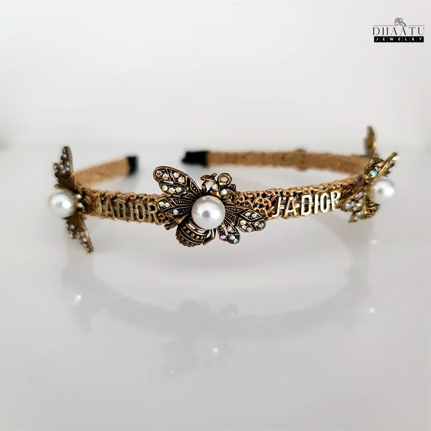Close-up of a golden bee and pearl embellished J'ADORE headband on a white background, highlighting intricate details and crystal sparkle