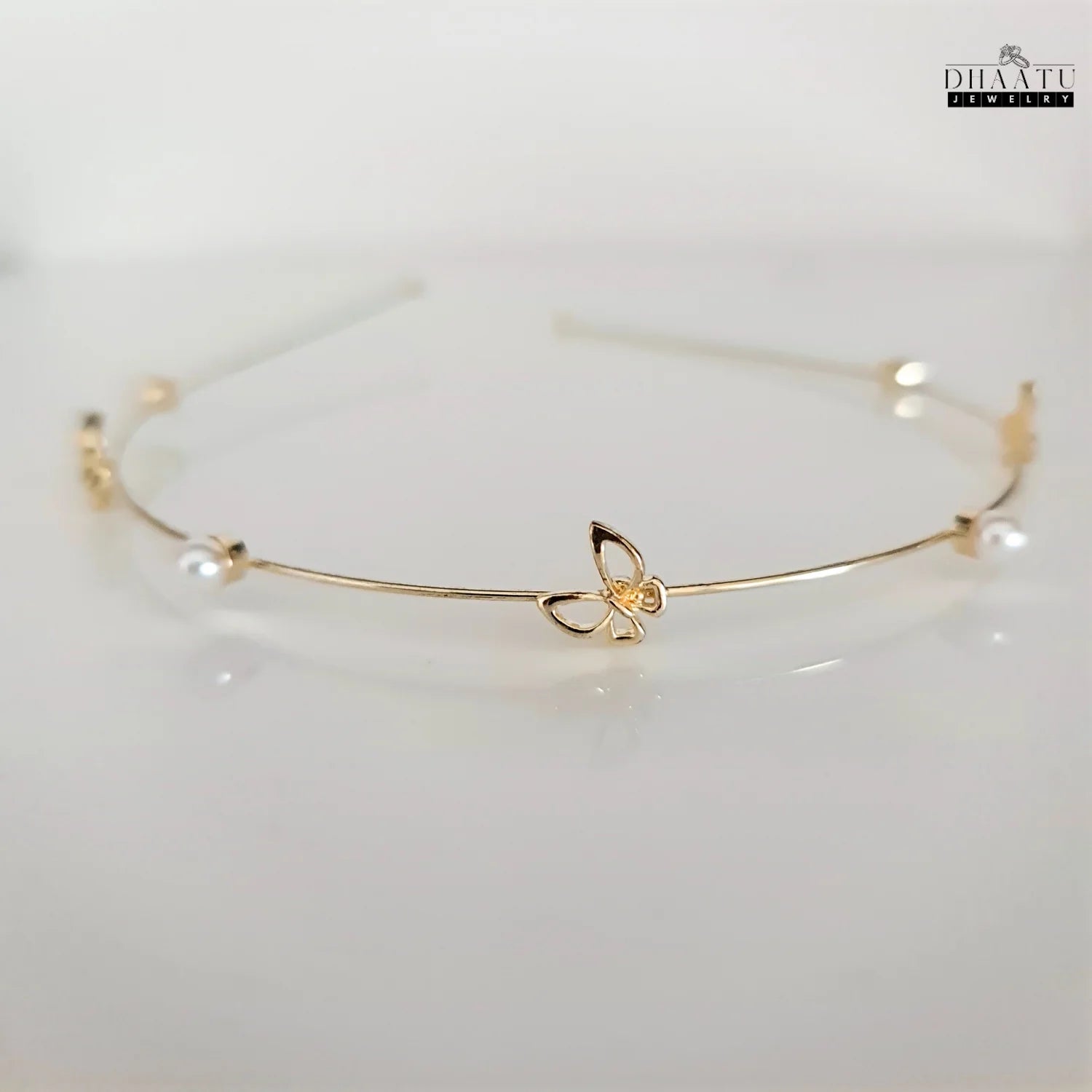 Front view of golden butterfly and pearl embellished modern hairband by Dhaatu Jewelry, showcasing intricate details and lustrous pearls on a white background