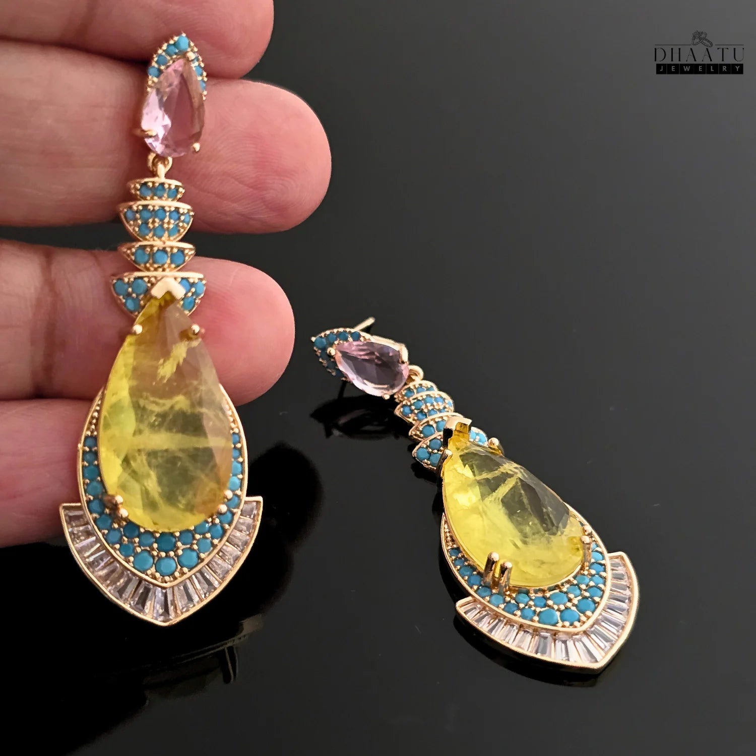 A hand holding one of the yellow stone dangle earrings, showcasing its size and intricate craftsmanship.