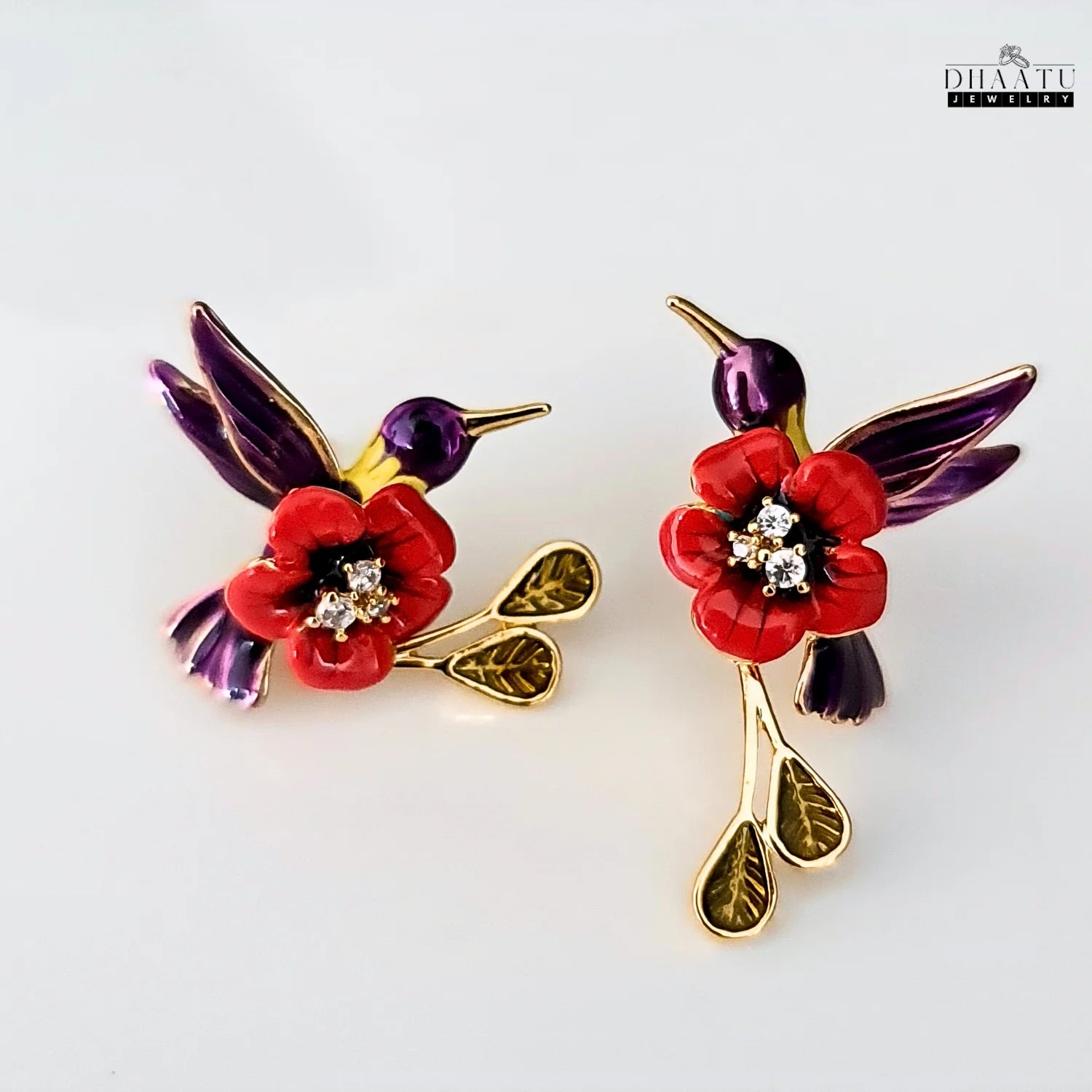 A pair of red and purple enamel hummingbird earrings with a red flower and hanging leaves on a white background.
