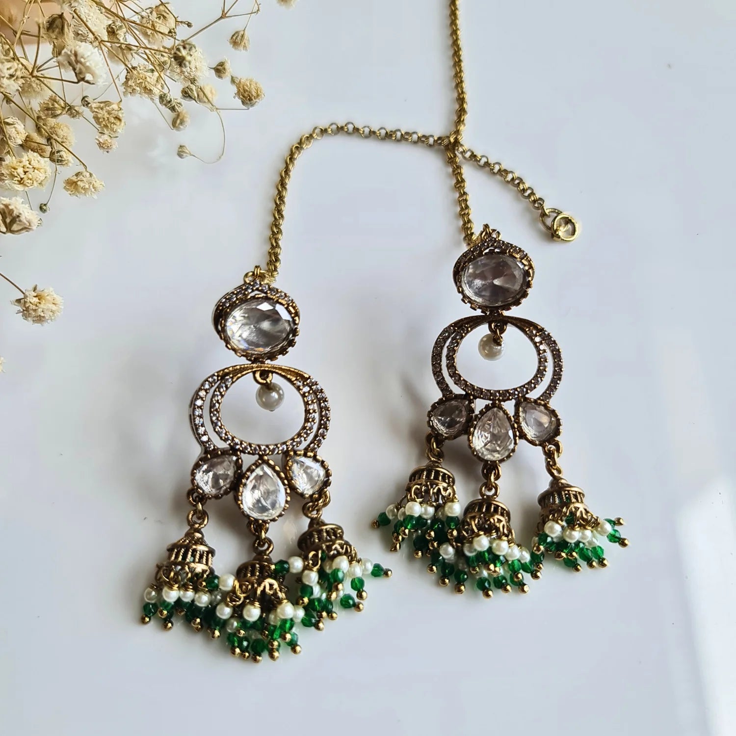 Festive Kundan Jhumka earrings featuring green and white pearl bead drops, accompanied by an ear chain on a white background.
