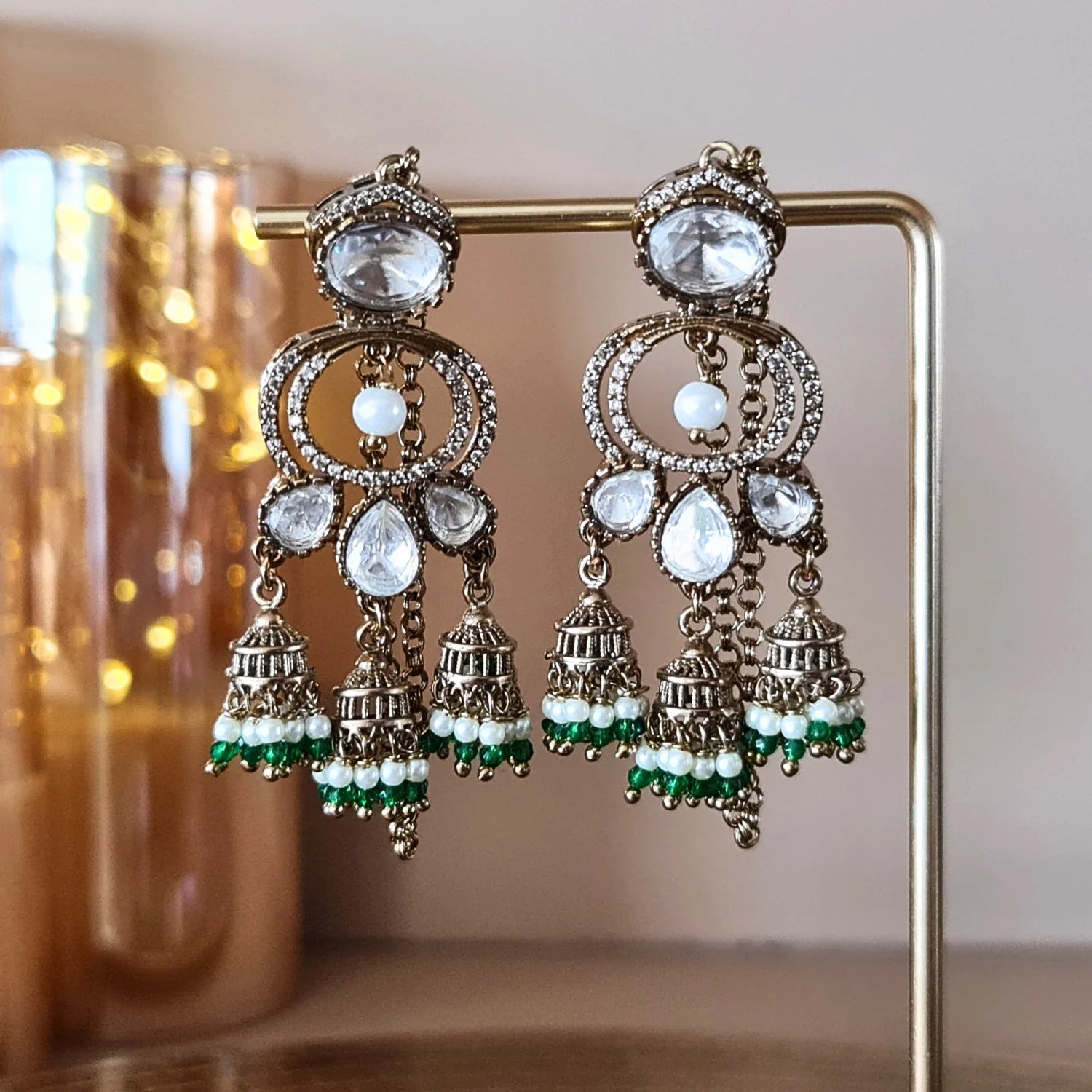 Stunning Kundan Jhumka earrings with bright green and white pearl bead drops, displayed on a gold jewelry stand.




