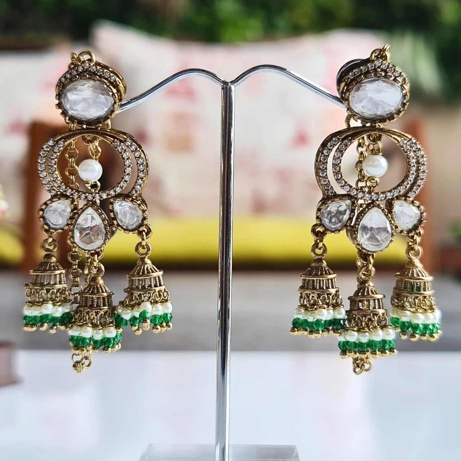 Exquisite Kundan and pearl jhumka earrings with green bead accents, presented on a silver jewelry stand.


