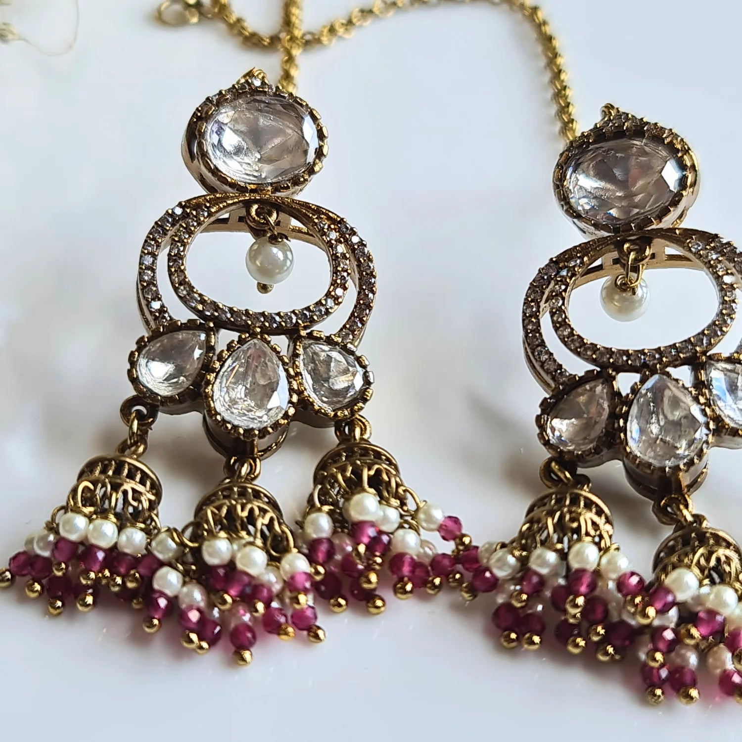 Close-up of ornate Kundan Jhumka earrings with rich maroon and white pearl bead drops and a delicate ear chain.

