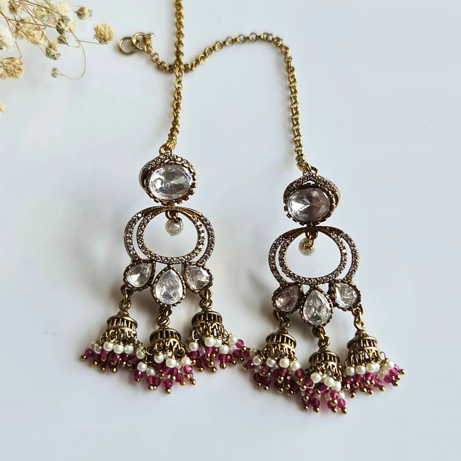 Festive Kundan Jhumka earrings featuring deep pink and white pearl bead drops, accompanied by an ear chain on a white background.

