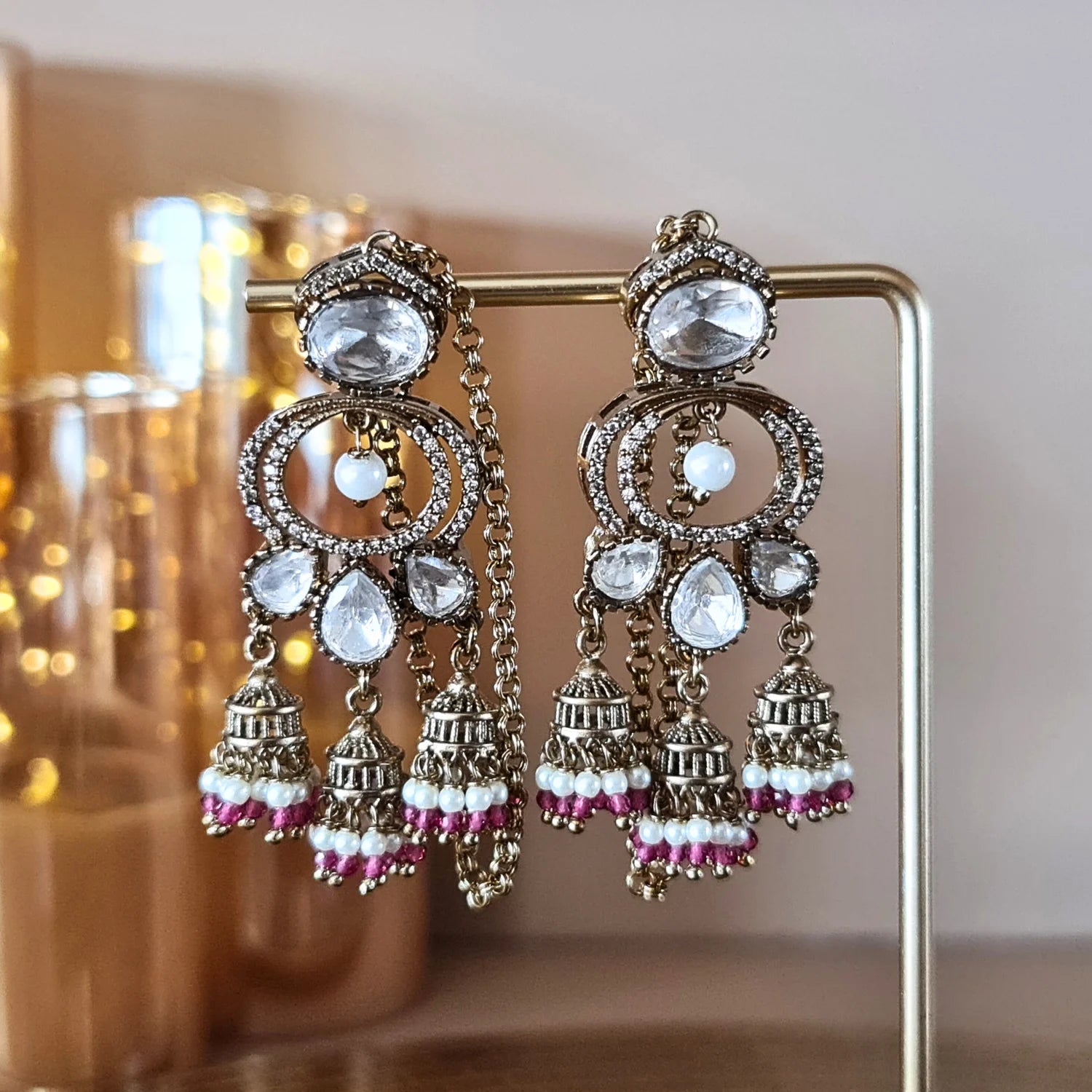 Exquisite Kundan and pearl jhumka earrings with maroon bead accents, presented on a silver jewelry stand.

