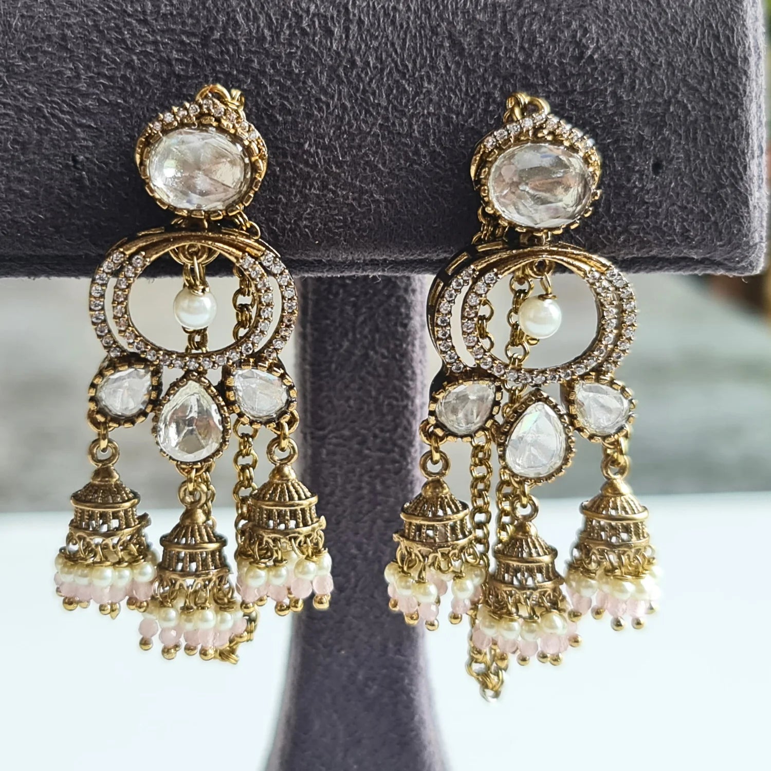 Pair of classic Kundan Jhumka earrings with light pink and white pearl beads, presented on a dark grey velvet jewelry display.
