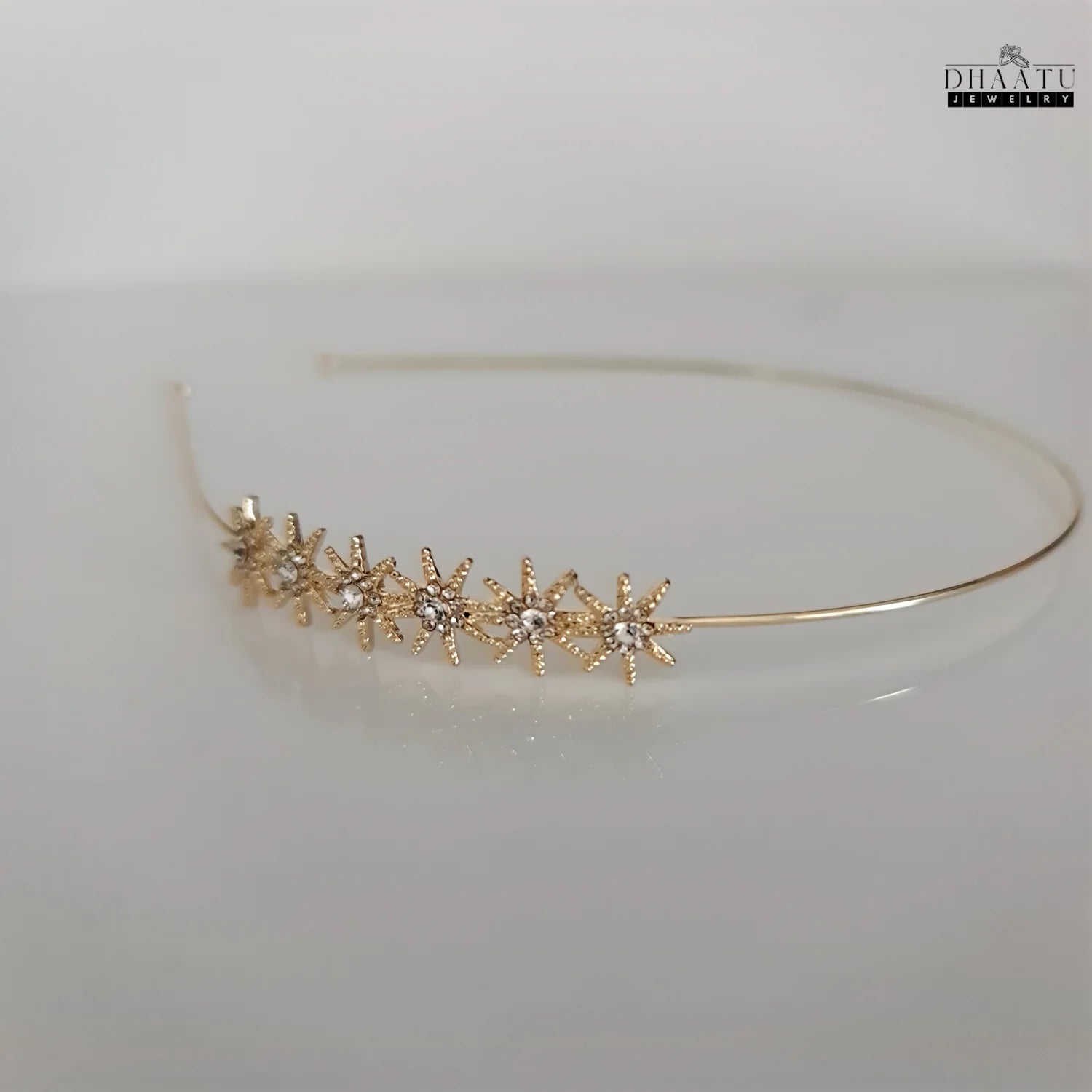 Side view of a modern cubic zirconia starburst hairband in gold tone on a light background, highlighting its elegant design.