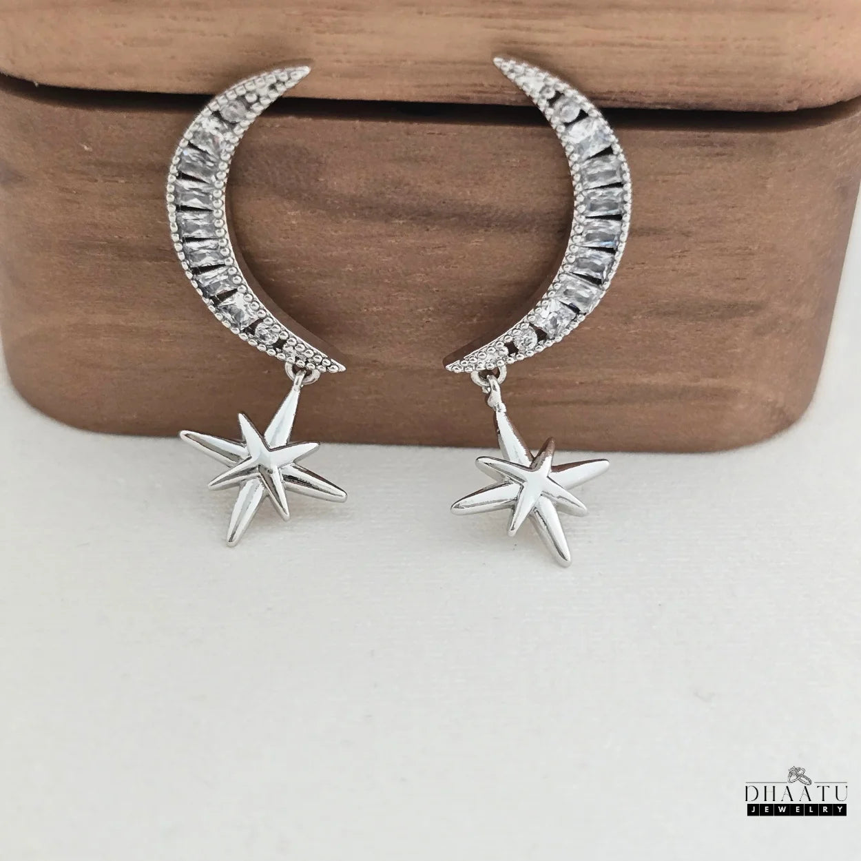 Pair of rhodium-plated moon and star dangle earrings with zircon stones, presented on a light background