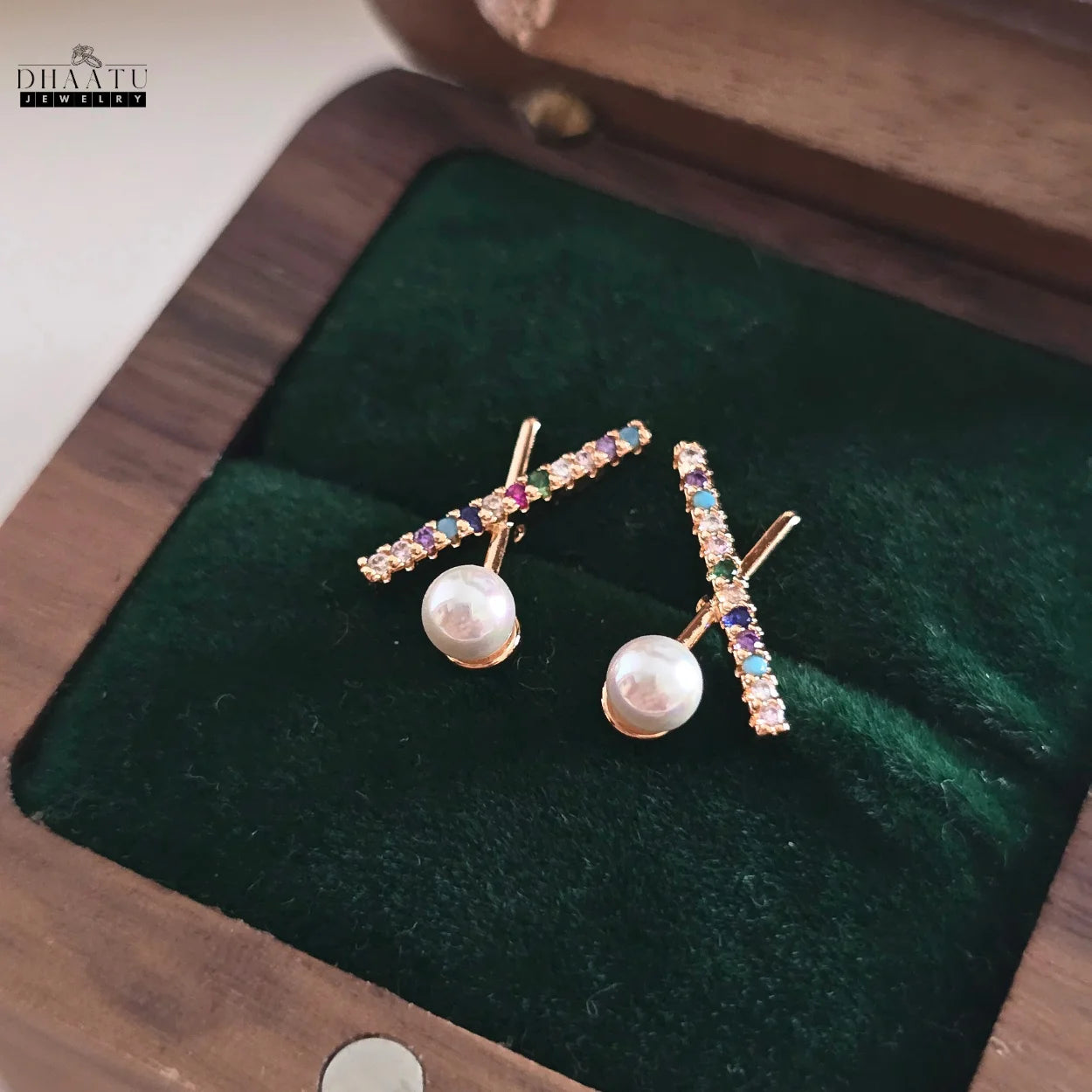 Dhaatu Jewelry multicolor zircon and pearl X stud earrings resting in a dark green velvet-lined wooden jewelry box