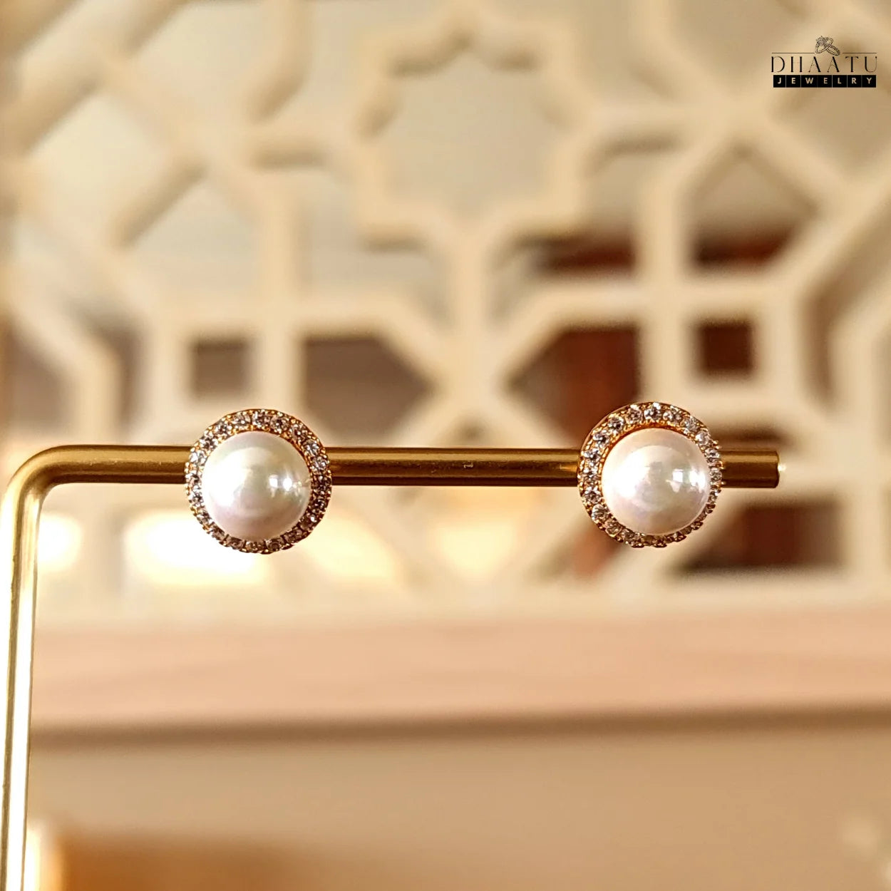 Pearl and zircon halo stud earrings displayed on a gold jewelry stand with a decorative background.