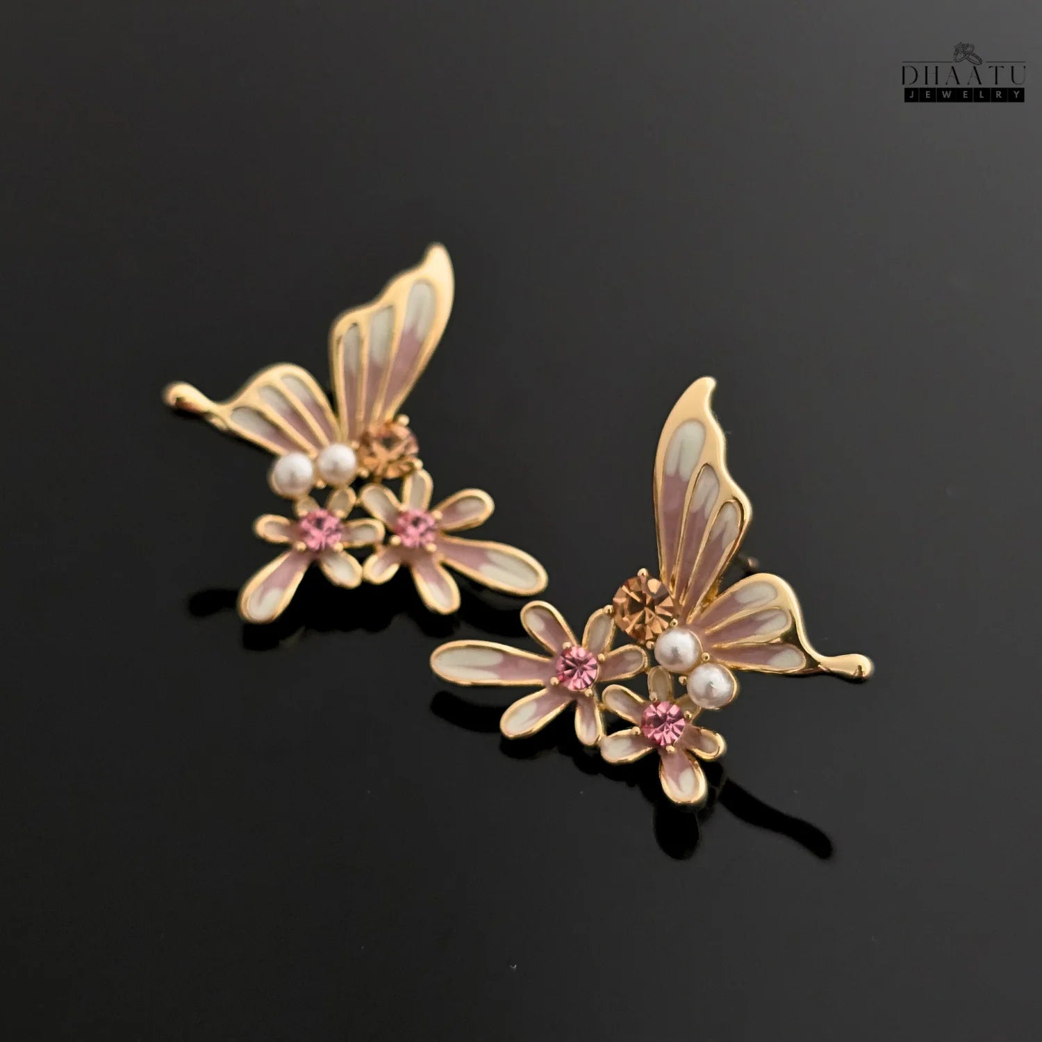 Pair of pink and white butterfly and flower stud earrings on a dark reflective background.