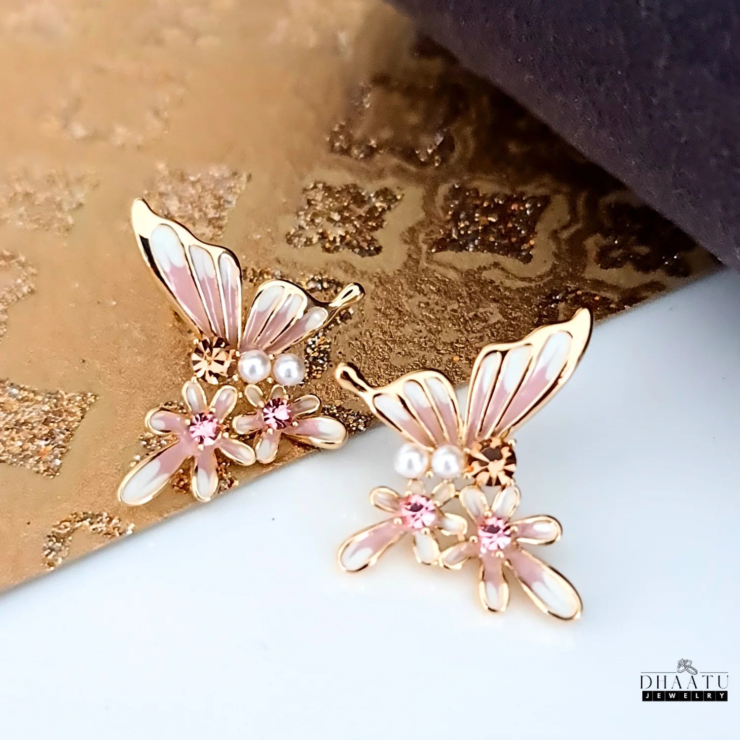 Pair of pink and white butterfly and flower stud earrings on a gold textured background.