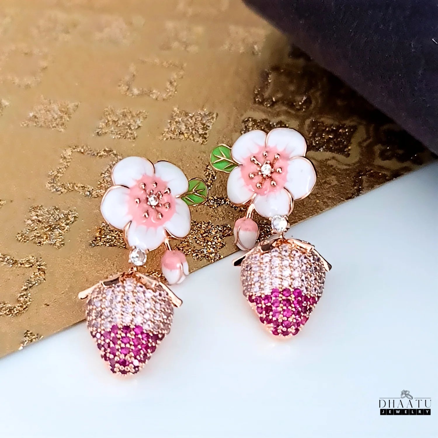 Floral-themed strawberry earrings with pink and white flowers on a textured surface