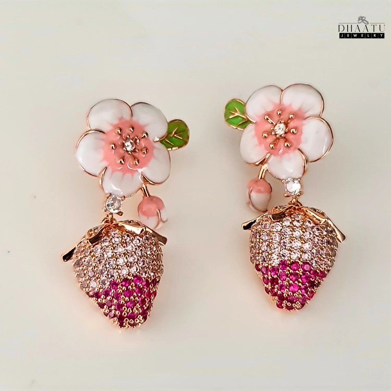 Strawberry-themed earrings with floral designs on a light background, branded 'Dhaatu'.