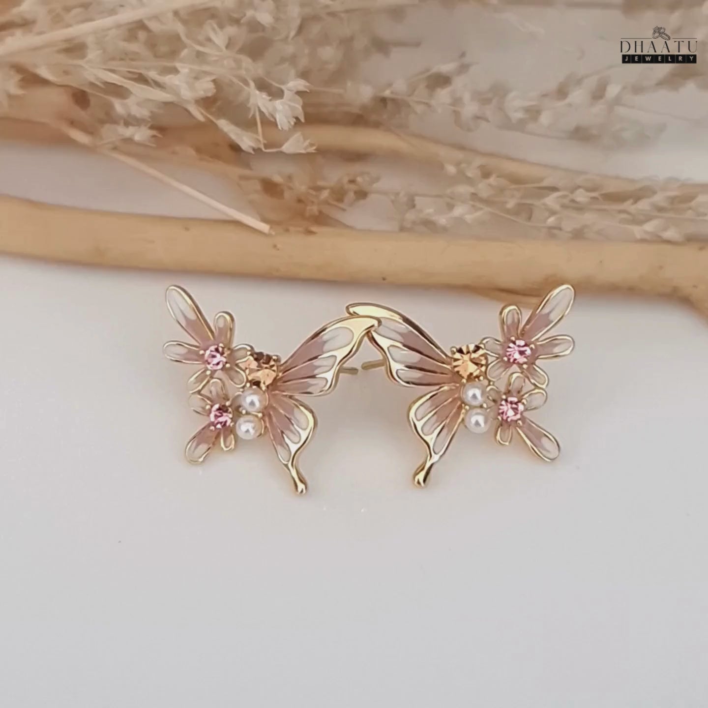 Load video: Video showcasing the pink and white butterfly and flower stud earrings with pearl and crystal details on white background.