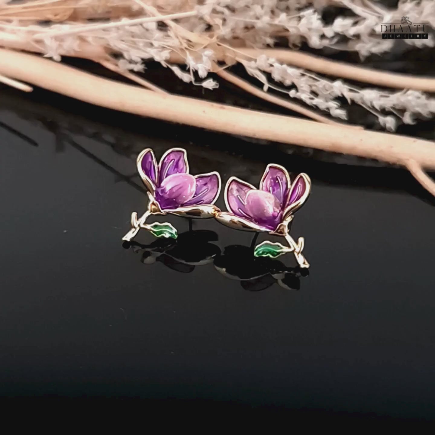 Load video: Product video of a pair of Dhaatu Jewelry purple enamel floral stud earrings shown against a black reflective background, highlighting their elegant design and glossy finish.