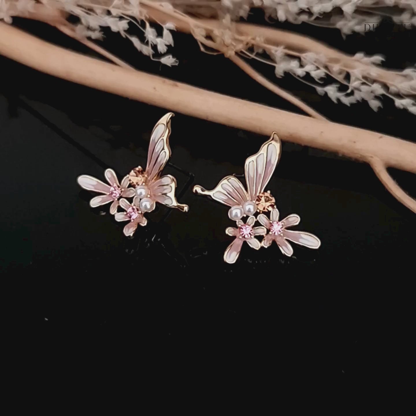 Load video: Video showcasing the pink and white butterfly and flower stud earrings with pearl and crystal details on black background.