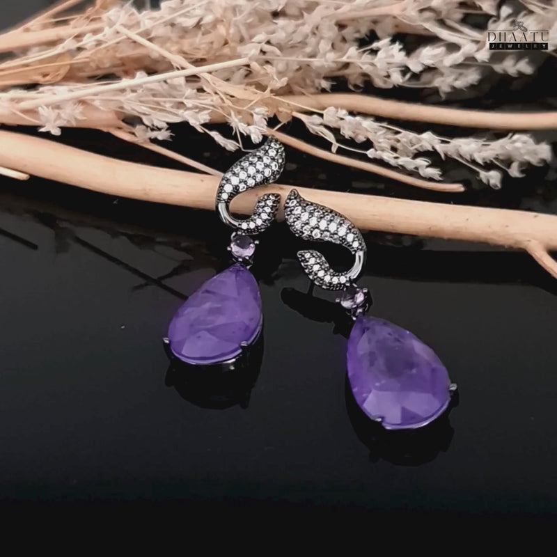 Video of Dhaatu Jewelry amethyst purple stone dangle earrings with zircon plating on a black reflective background.

