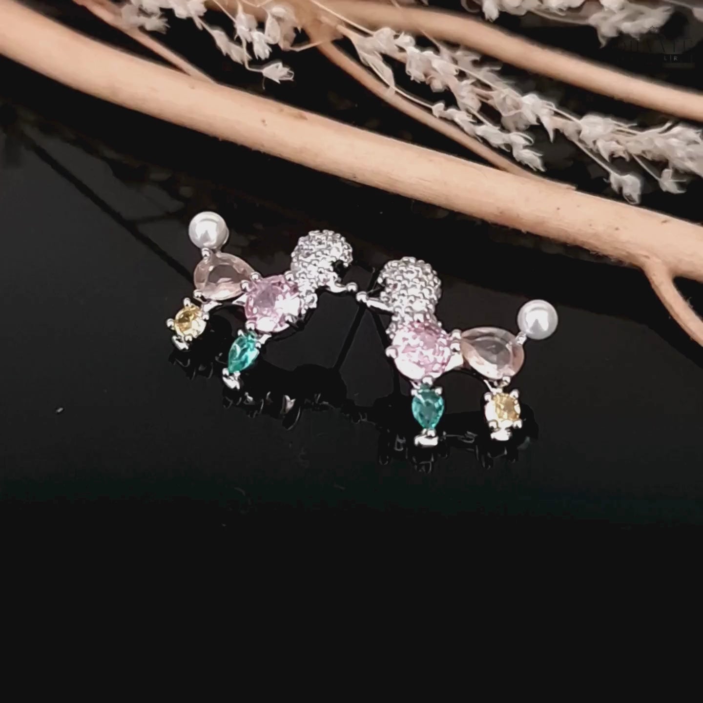 Load video: Video showcasing the pastel-colored poodle earrings with faux pearls and crystals on a dark surface.