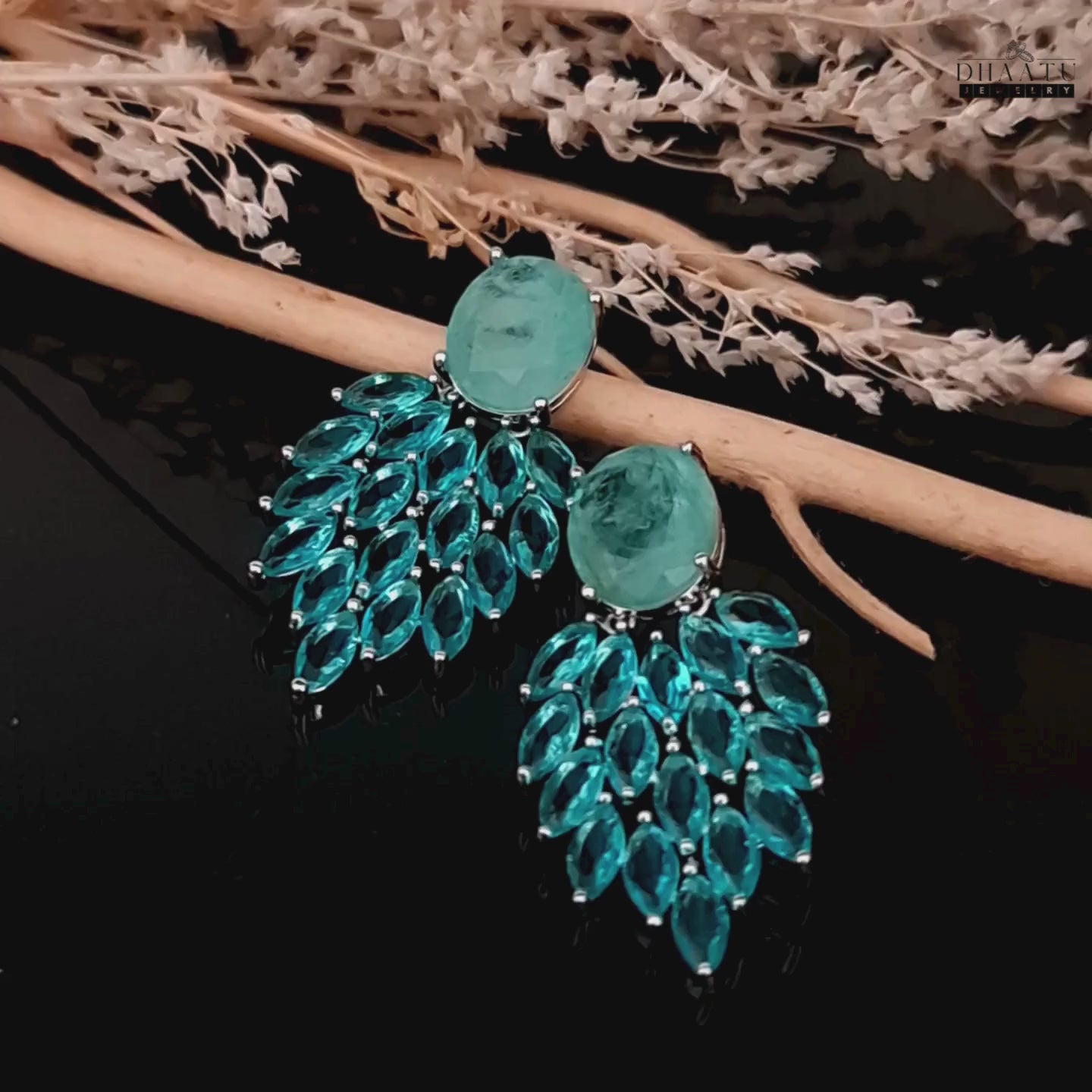 Load video: A video showcasing the movement and sparkle of the Aqua Chalcedony and marquise cut blue stone dangler earrings against a dark background with decorative branches.
