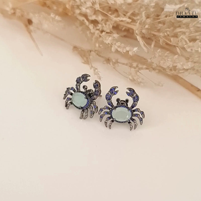 A video showcasing the silver-toned crab earrings from multiple angles, highlighting the dark blue and aquamarine zircon stones.