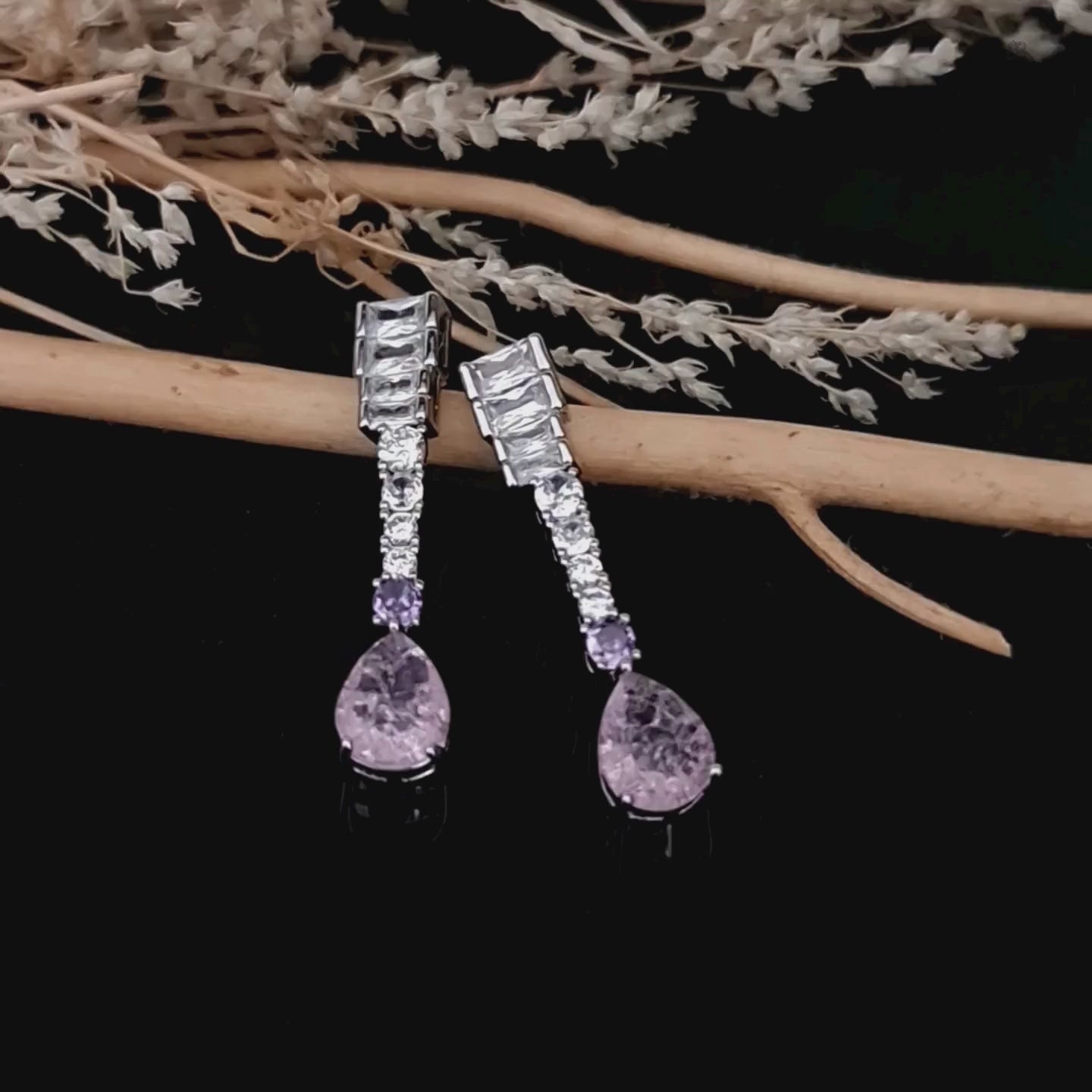 Load video: Product video of Silver-toned Zircon drop earrings with pink and lilac stones on a glossy black background