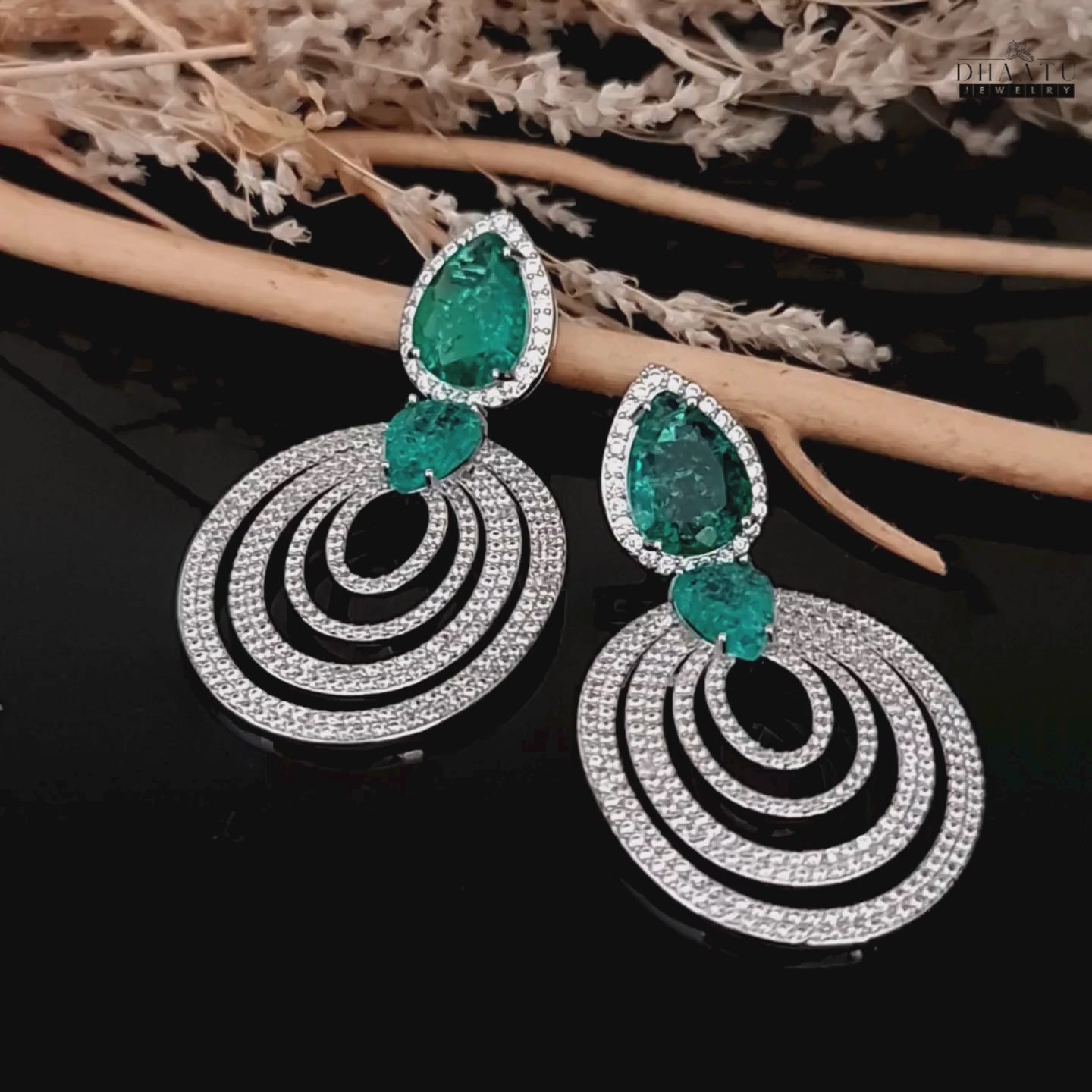 Load video: A short video showcasing the sparkle and movement of the DHAATU JEWELRY emerald green and pave diamond chandelier earrings on a black background with decorative sticks.