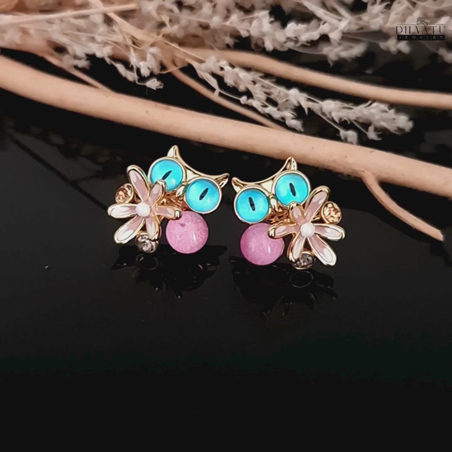 Load video: Video showcasing the Dhaatu Jewelry owl earrings with blue eyes and pink gemstone, set against a natural decor.