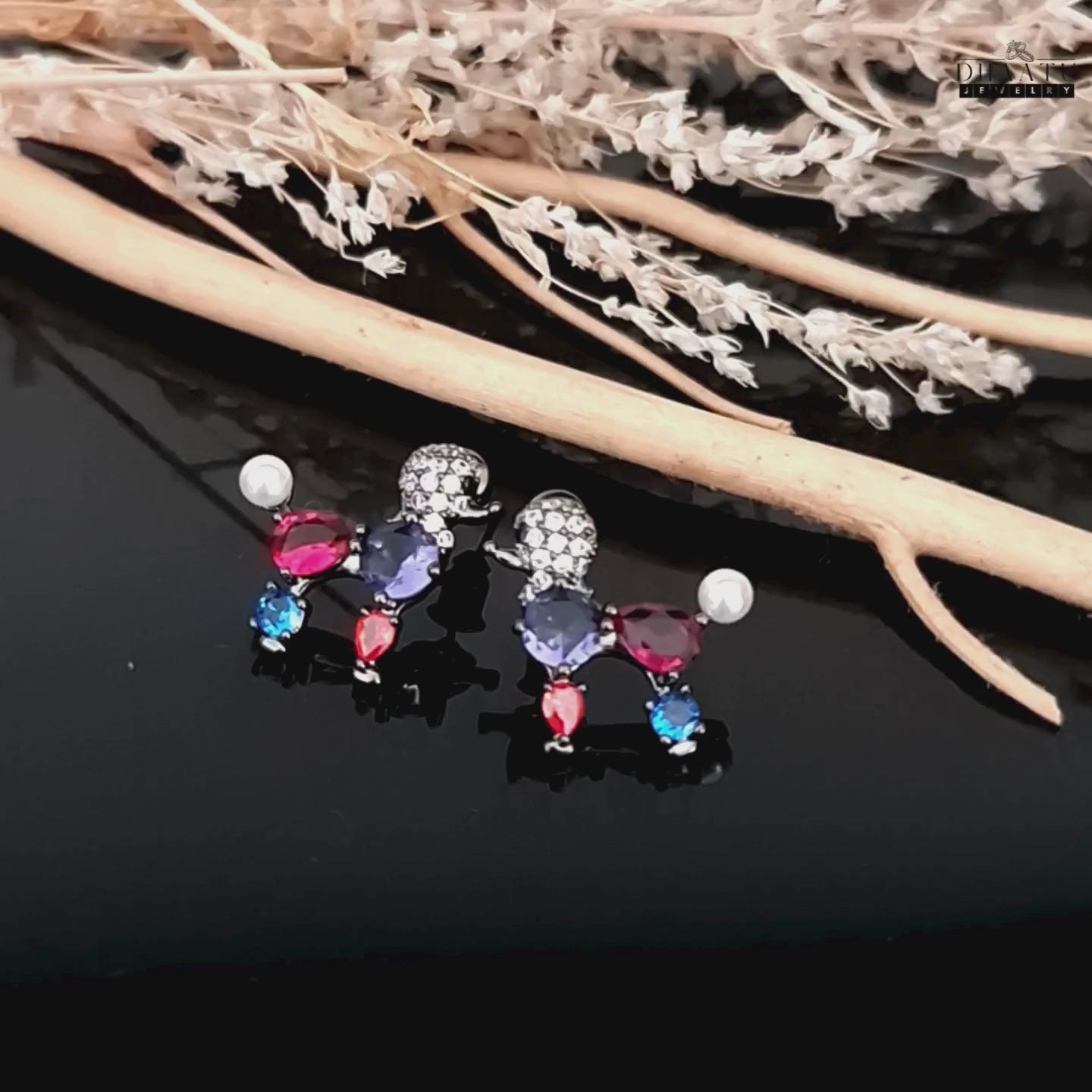 Load video: Video showing the multicolor poodle earrings with vibrant red, blue, and purple crystals on a dark background.