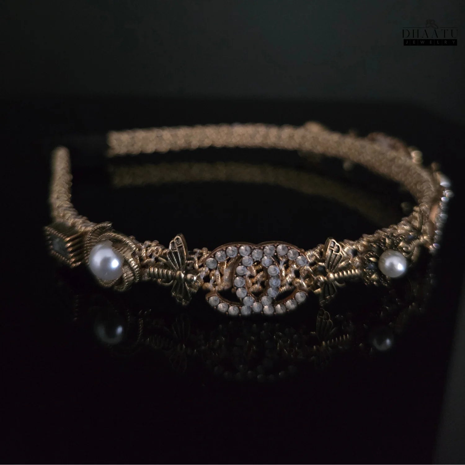 Side angle of a regal gold and pearl embellished crystal hairband on a dark surface, emphasizing the golden braid and decorative elements
