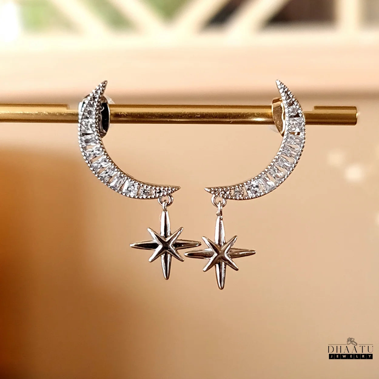 Rhodium-plated moon and star dangle earrings with sparkling zircon stones hanging from a gold bar, emphasizing their brilliance