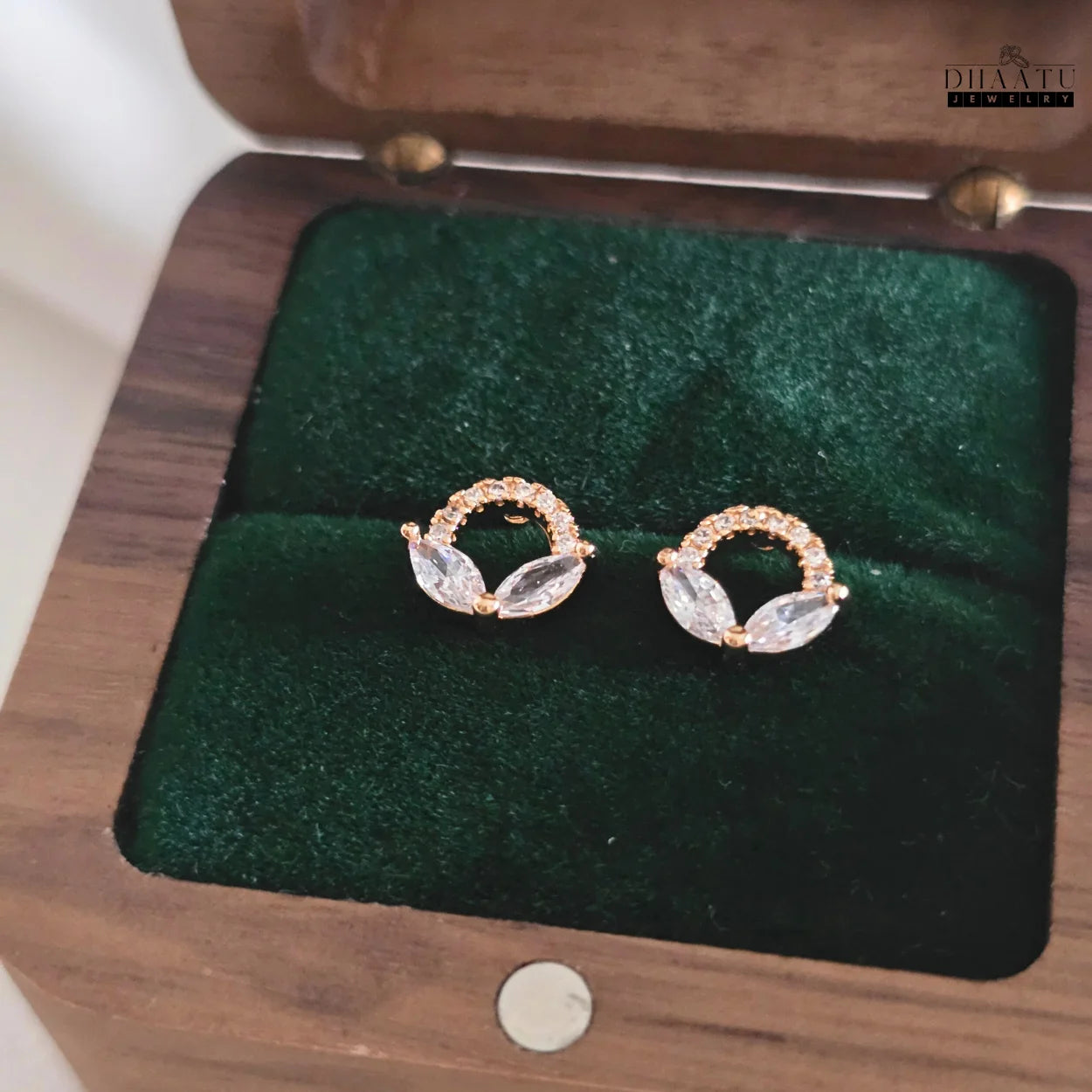 Close-up of rose gold plated marquise and pavé cubic zirconia stud earrings resting in a dark green velvet-lined wooden jewelry box.