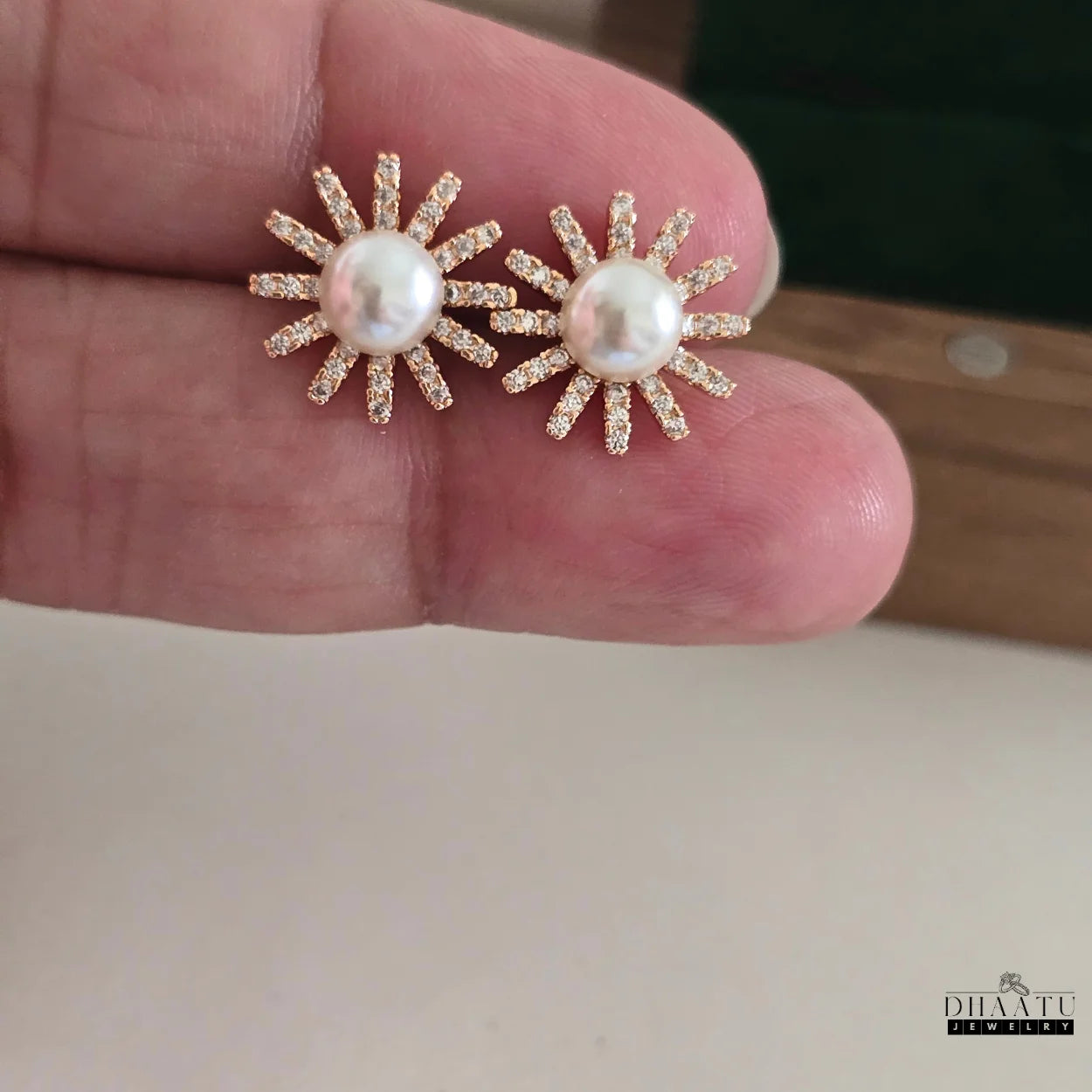 Rose gold-plated sunburst stud earrings with pearls and zircons held in hand, showing their size and detail.

