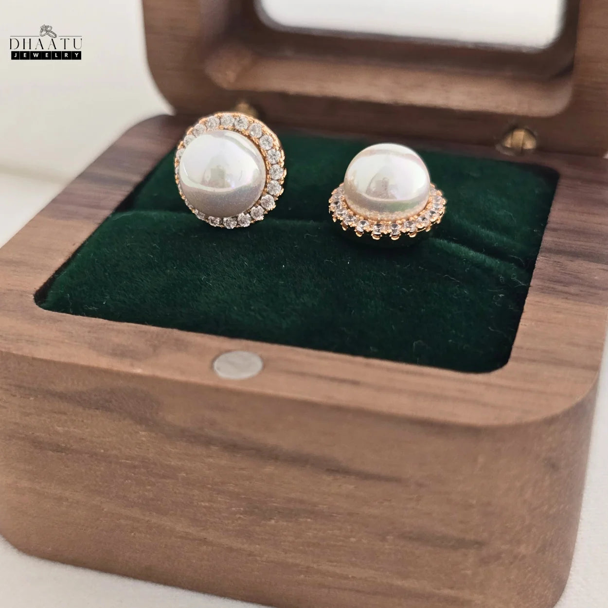 Close-up of rose gold plated pearl and zircon halo stud earrings resting in a wooden jewelry box.