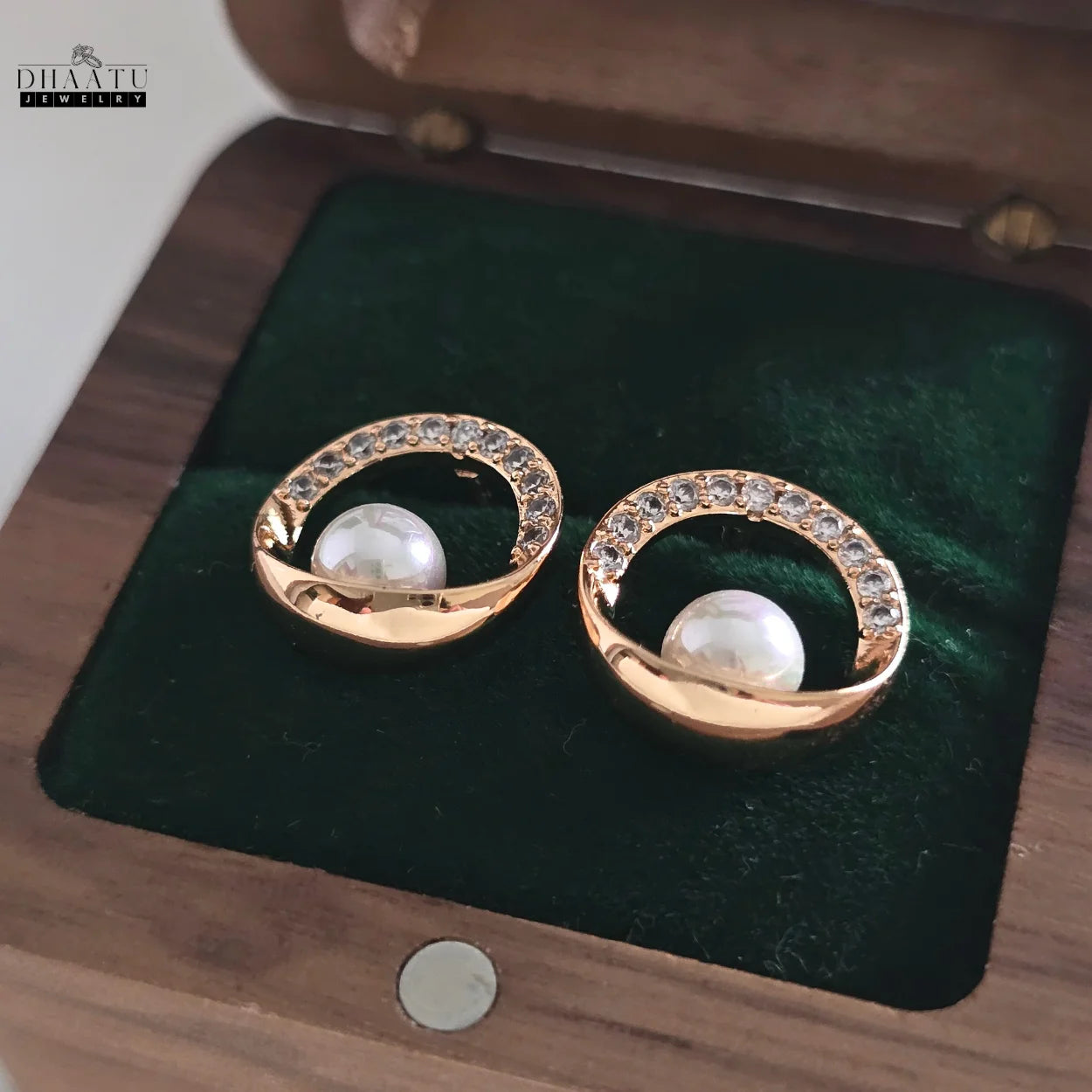 Pair of rose gold plated stud earrings with a pearl and zircon halo, resting in a dark green velvet-lined jewelry box, highlighting the detailed craftsmanship