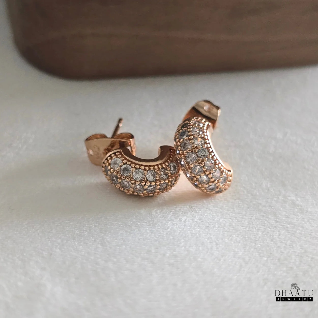 Close-up front view of two rose gold plated huggie hoop earrings with sparkling zircon pave, showcasing their intricate design and brilliant stones.