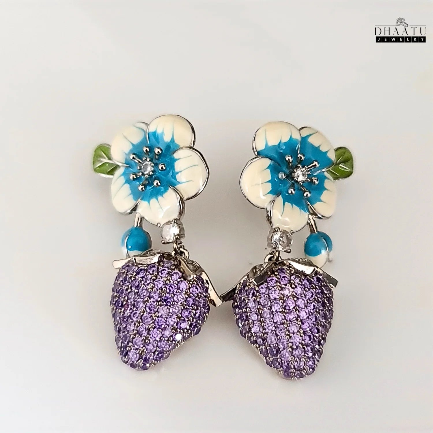 Pair of silver-plated drop earrings featuring white and blue enamel flowers with purple CZ strawberry charms, displayed on a white background.
