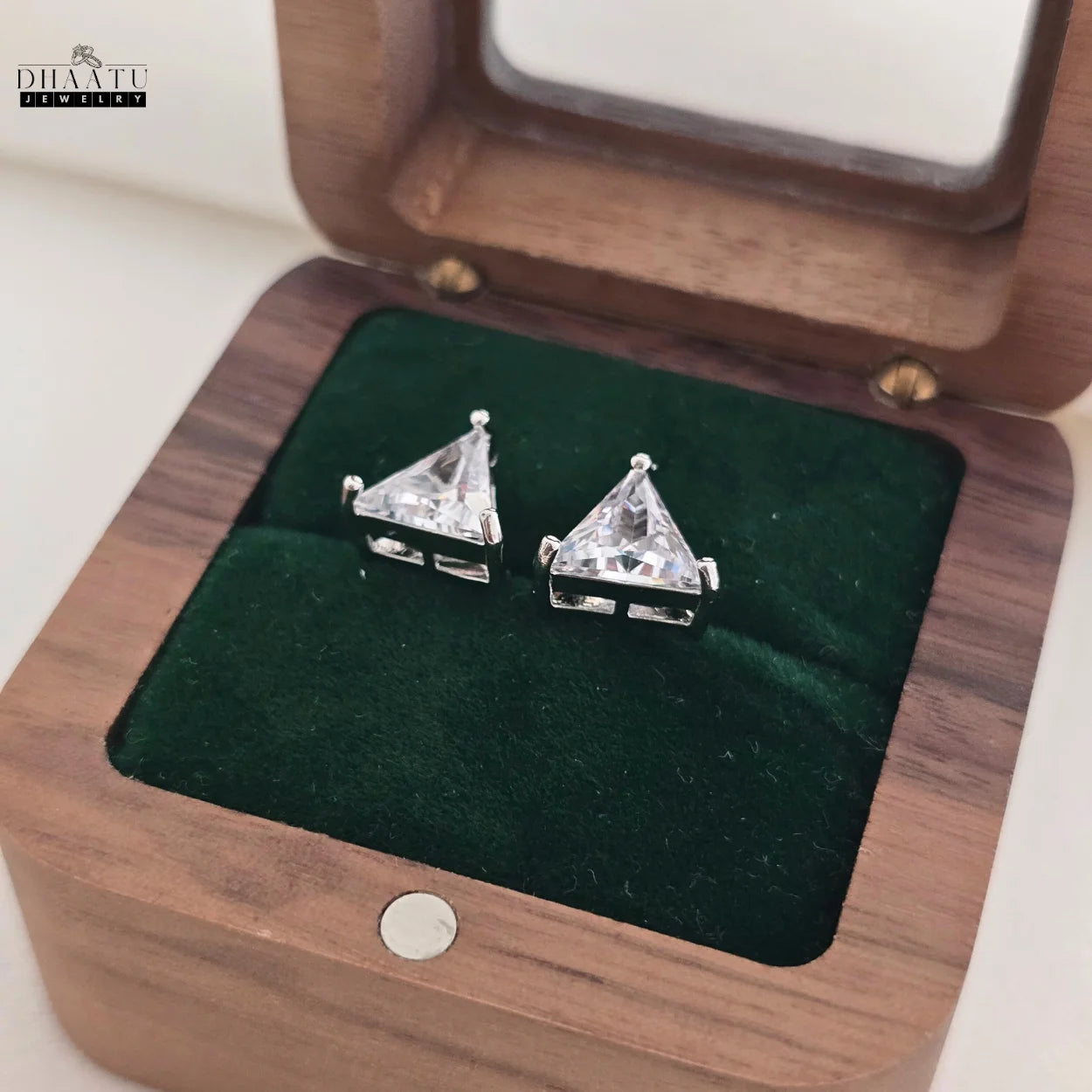 Pair of silver-plated triangle stud earrings with clear CZ stones displayed in a green velvet-lined wooden jewelry box