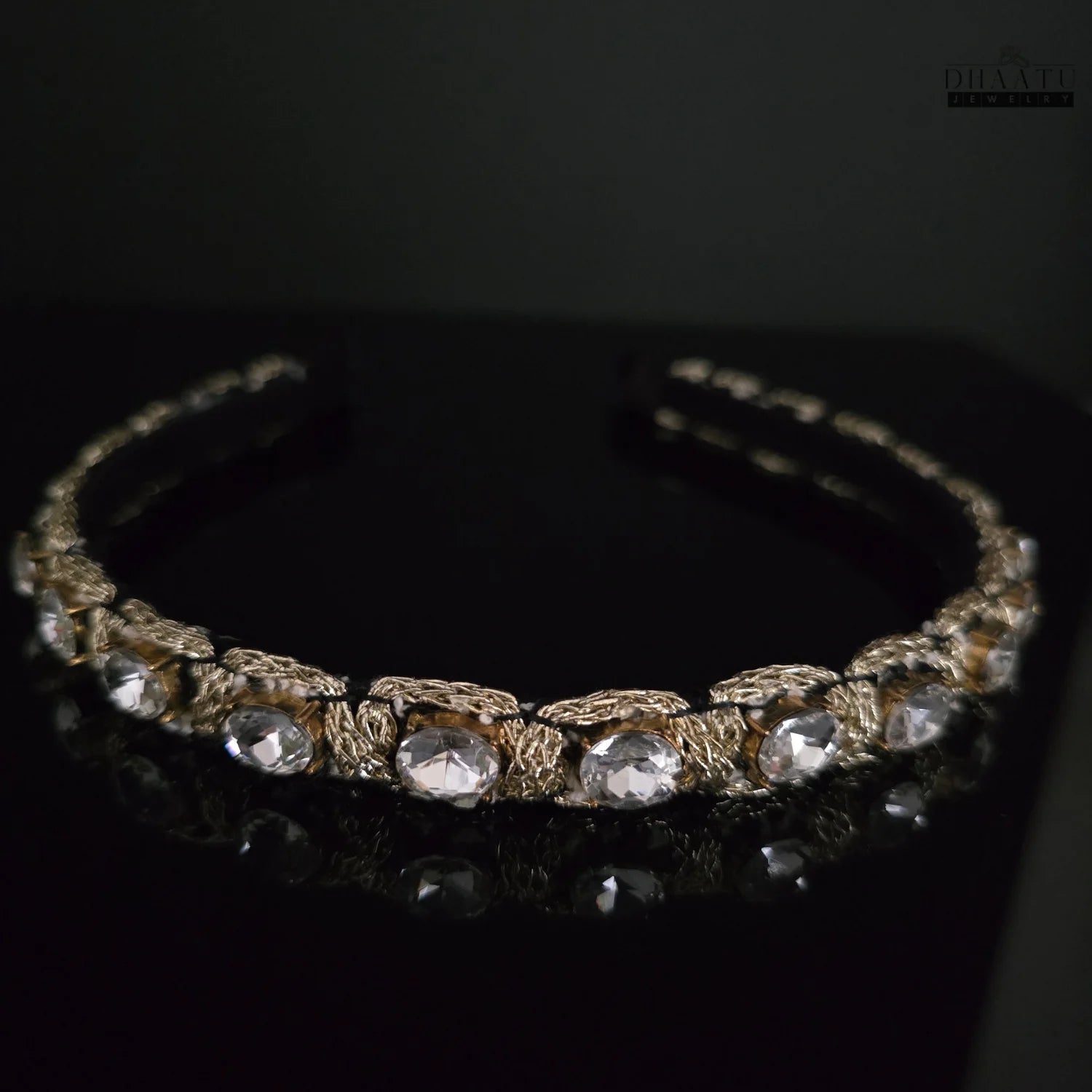 Close-up of a modern Western headband with clear crystals and golden woven detailing on a black background, reflecting light