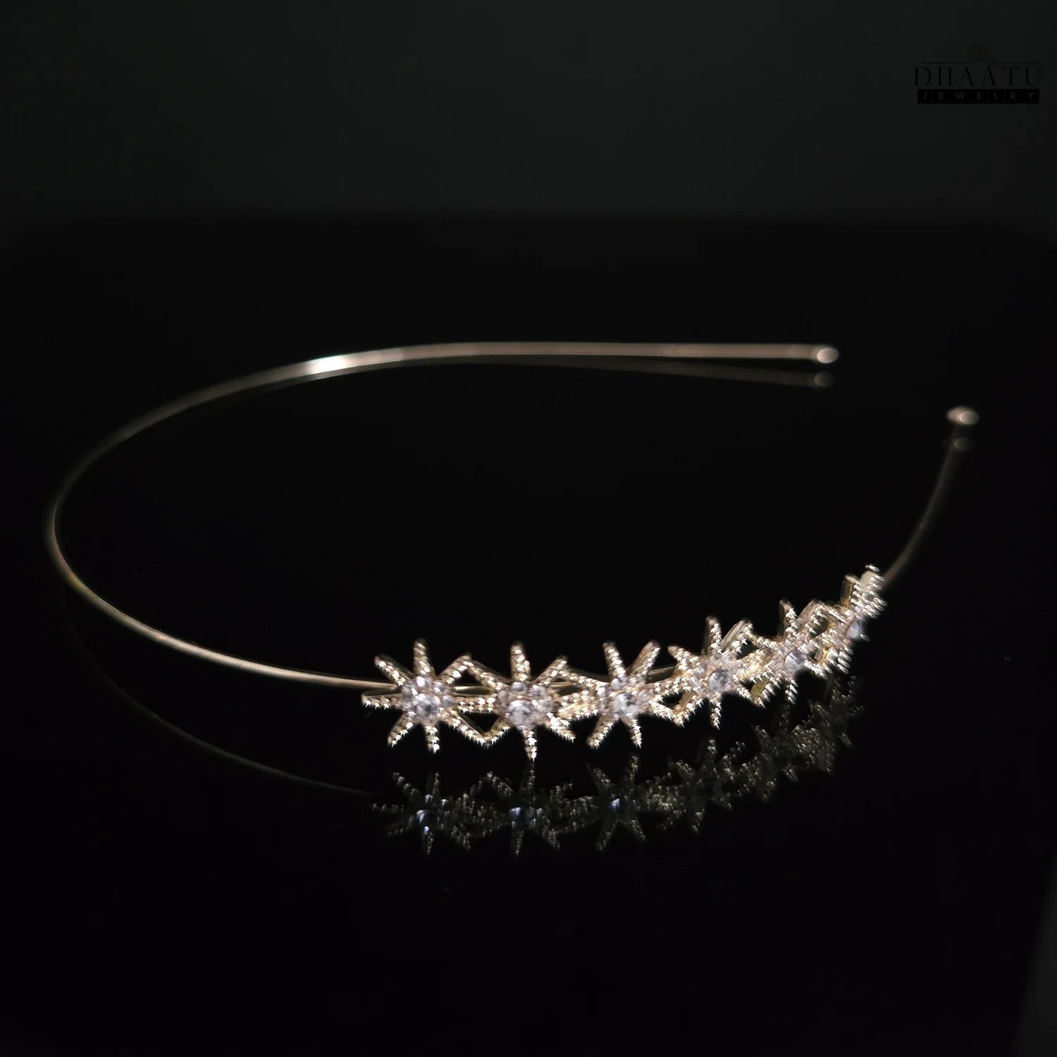 Close-up of a sparkling starburst zirconia gold-toned headband on a dark reflective surface, showcasing intricate details