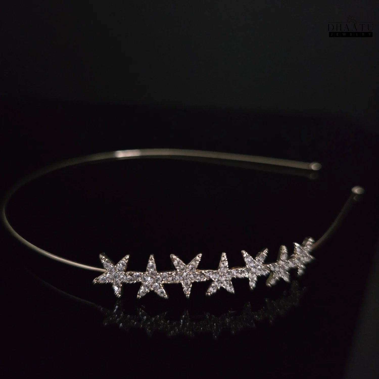 Close-up of sparkling starburst zirconia hairband on a dark background, showcasing individual star details and gold-tone finish.


