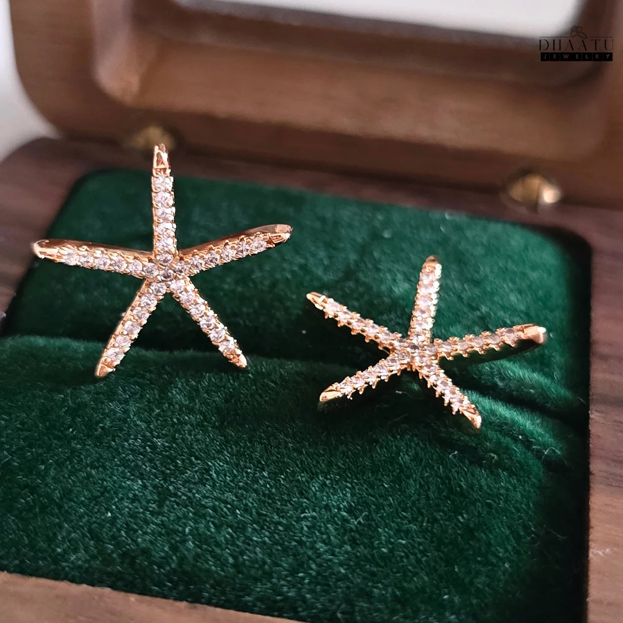 Close-up view of rose gold starfish stud earrings with zircon stones, partially in a wooden jewelry box.
