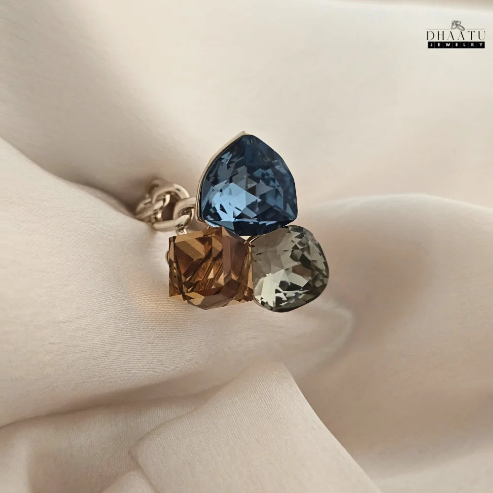 A stylish statement ring featuring blue, brown, and grey crystals on a white fabric background.