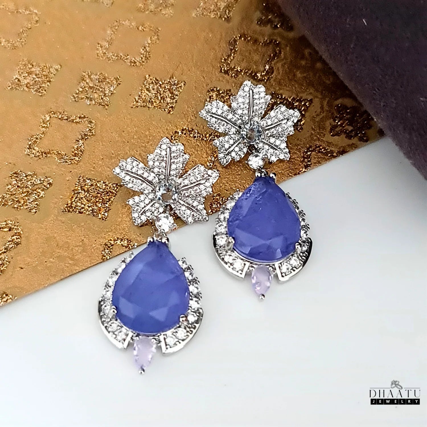A pair of elegant tanzanite and cubic zirconia earrings photographed on a decorative gold and brown background.
