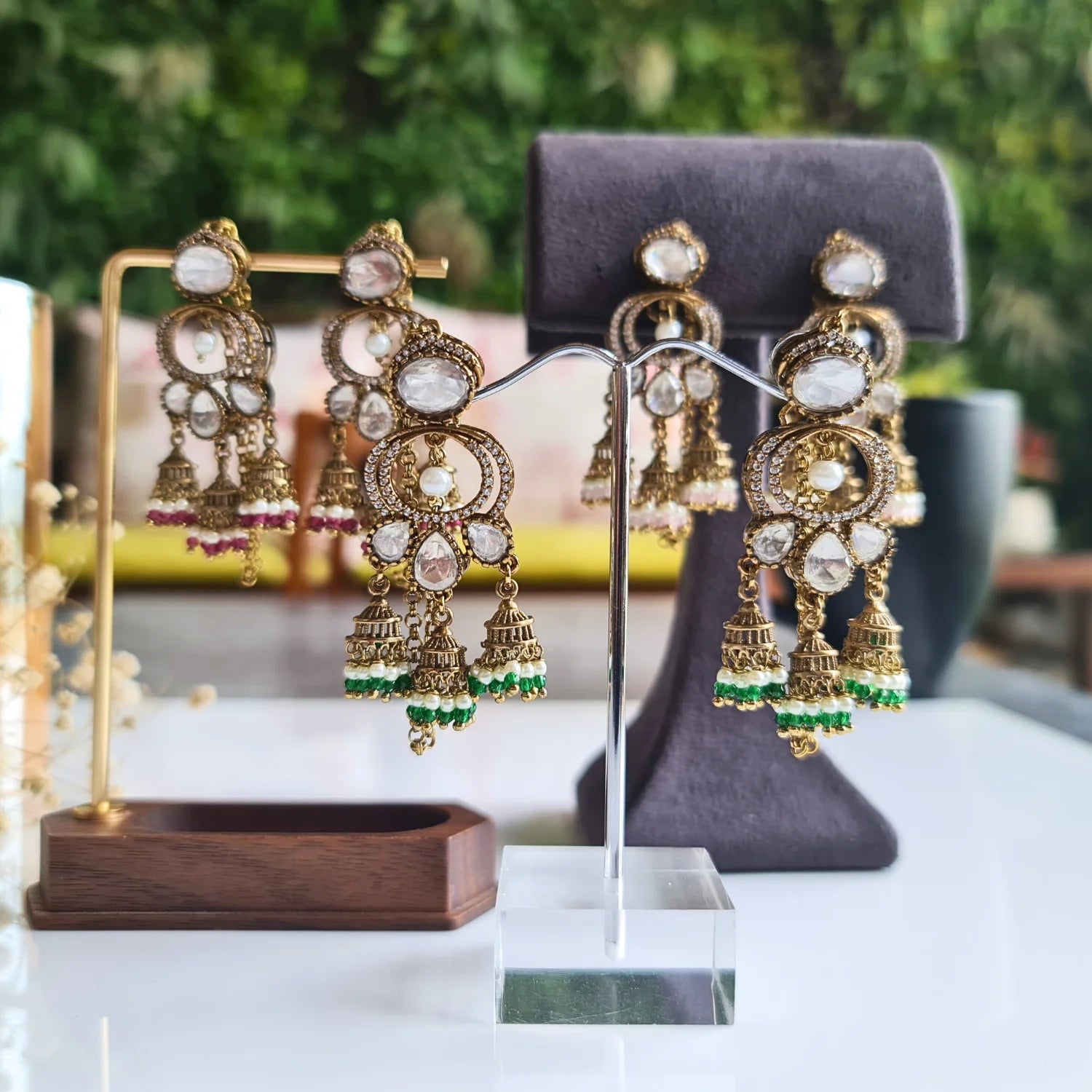 Festive Kundan Jhumka earrings featuring green, pink, marroon and white pearl bead drops, accompanied by an ear chain in an outdoor setting
